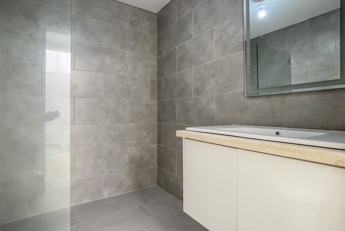 buyDRproperty Modern bathroom with gray tile and a glass shower in a Perla Marina condo. Sosua Real Estate