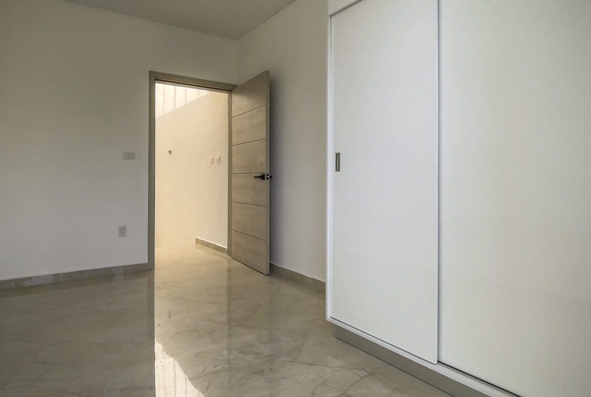buyDRproperty Empty modern condo bedroom with white walls, open door, and a closet. Sosua Real Estate