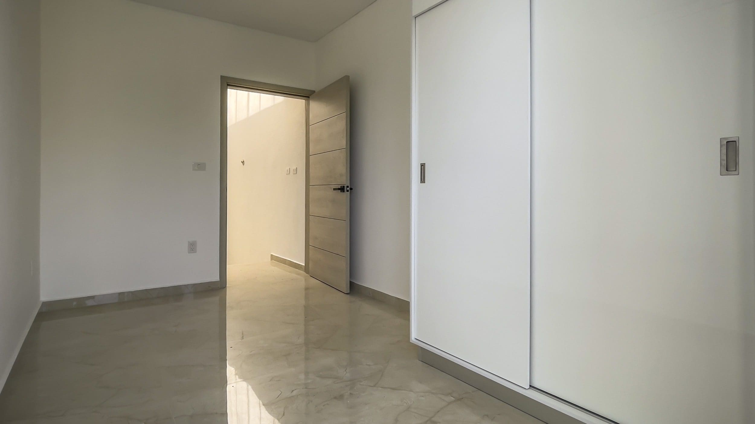 buyDRproperty Empty modern condo bedroom with white walls, open door, and a closet. Sosua Real Estate