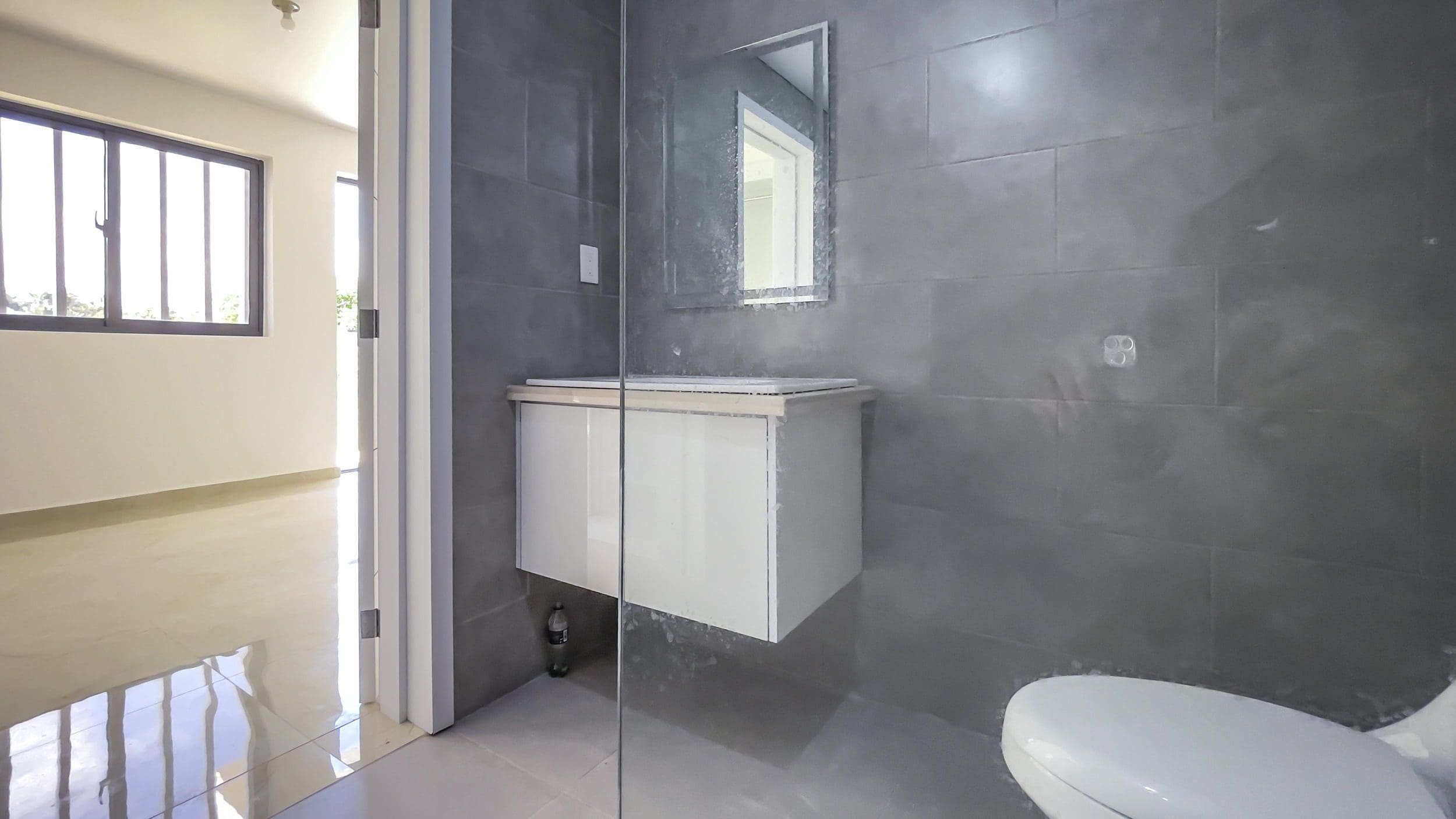 buyDRproperty Modern bathroom with gray tiled walls, white floating vanity, and mirror. For Sale! Modern 2 Bedroom Condo In Perla Marina. Sosua Real Estate