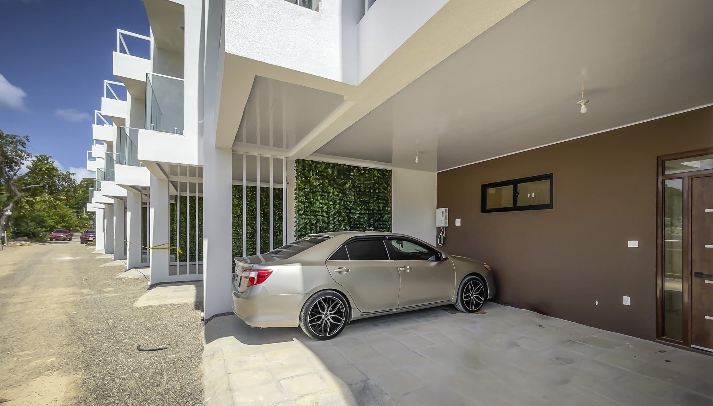 buyDRproperty Modern condo with gold sedan parked in covered parking area. Sosua Real Estate