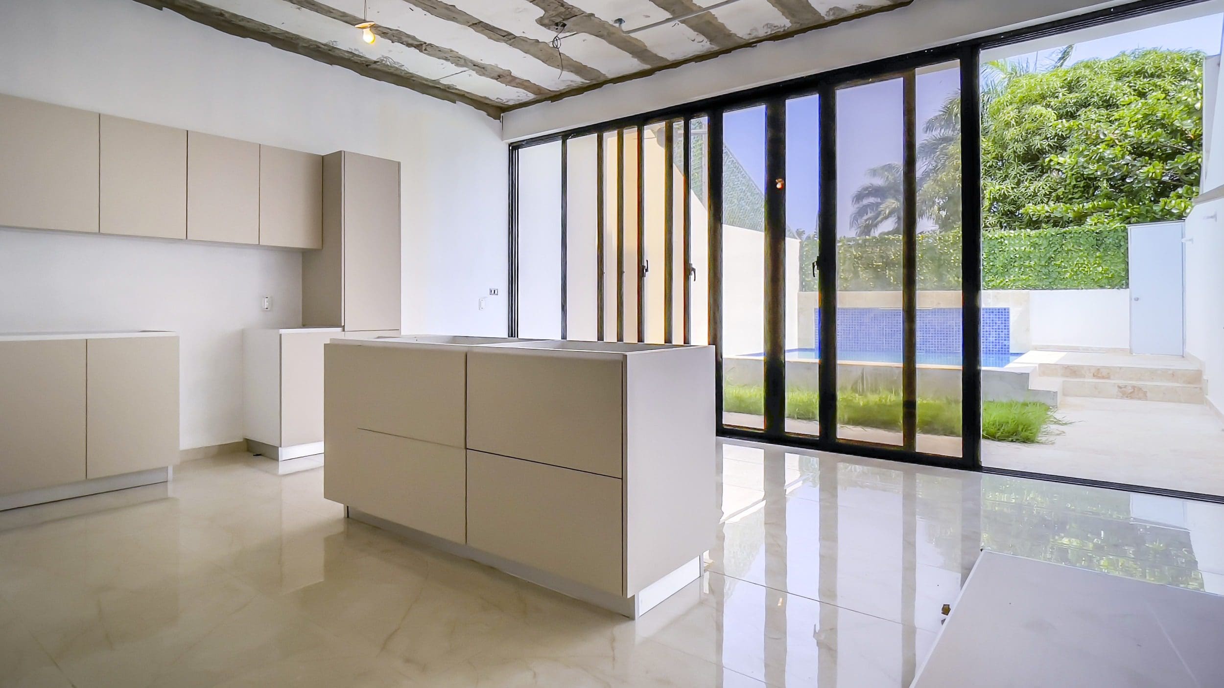 buyDRproperty Modern kitchen with neutral cabinetry, large sliding glass door, and outdoor patio with pool. Sosua Real Estate