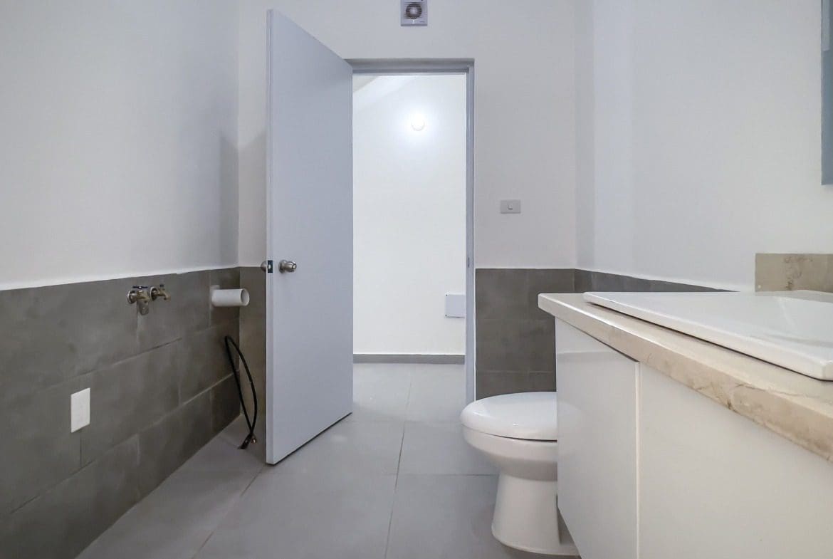 buyDRproperty Modern bathroom with toilet, sink, and open door in a Perla Marina condo. Sosua Real Estate