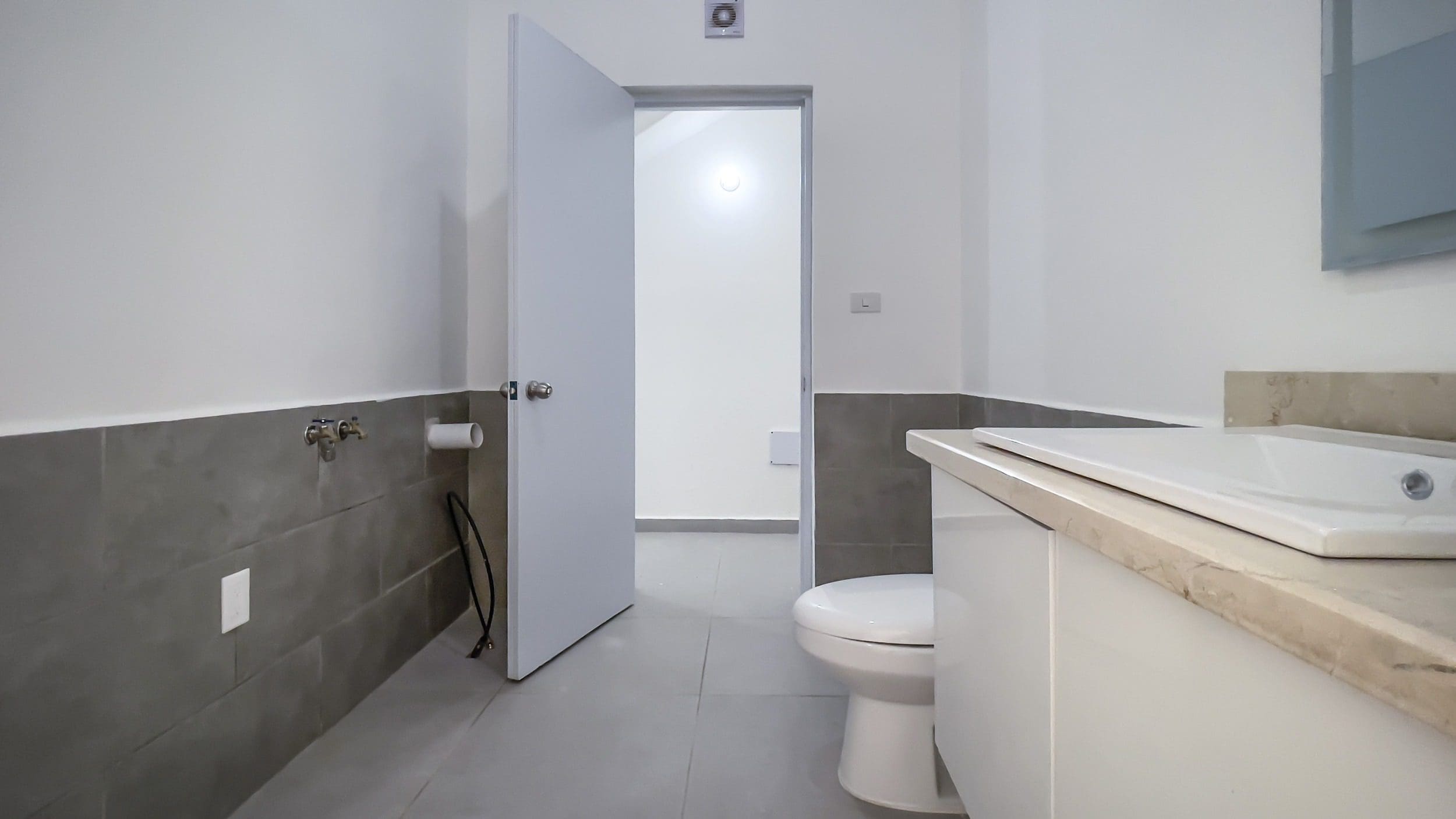 buyDRproperty Modern bathroom with toilet, sink, and open door in a Perla Marina condo. Sosua Real Estate