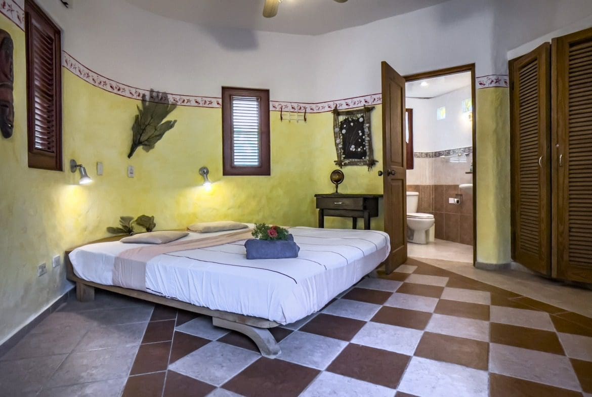 buyDRproperty Charming B&B bedroom with yellow walls and checkered tile floor. Sosua Real Estate
