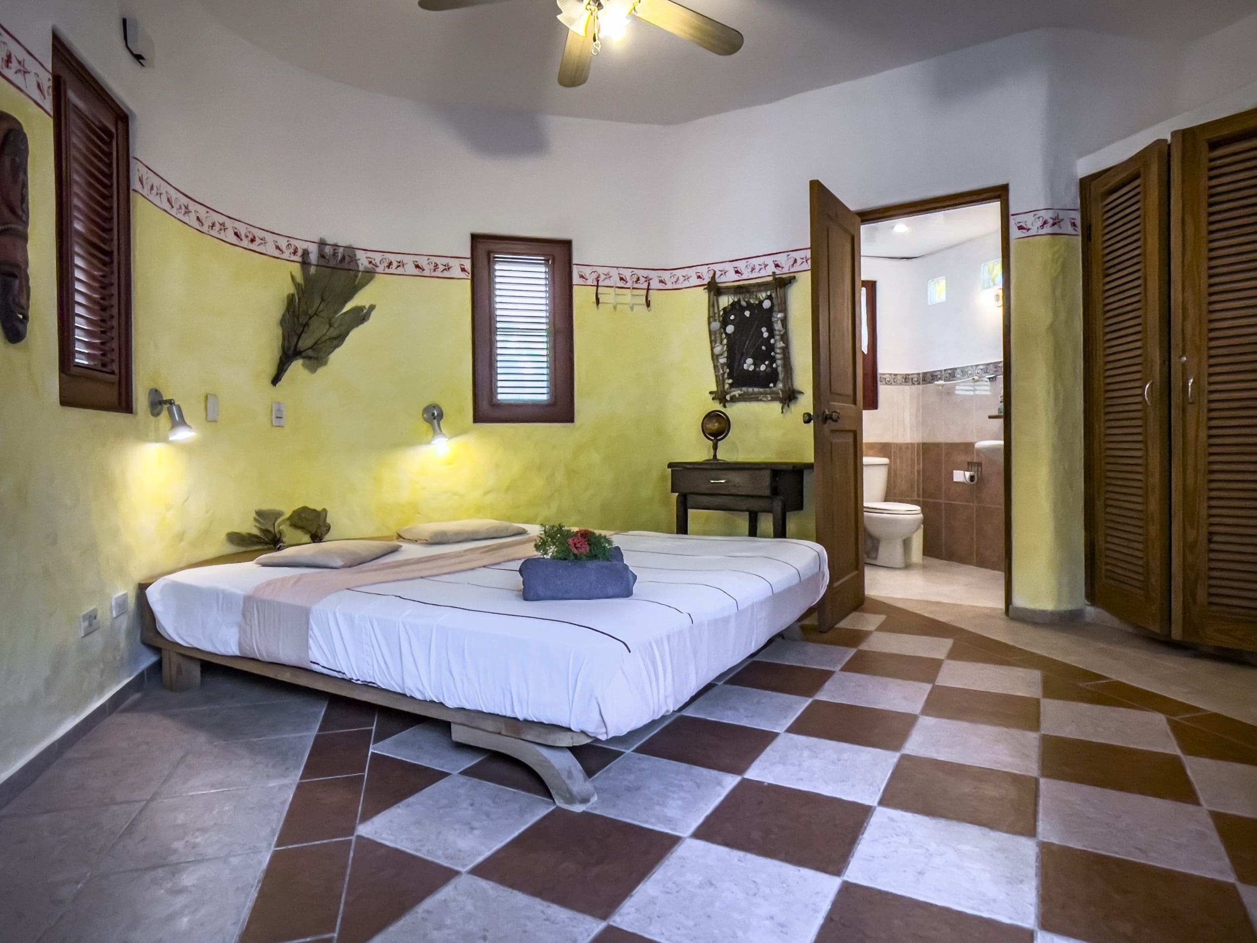 buyDRproperty Charming B&B bedroom with yellow walls and checkered tile floor. Sosua Real Estate
