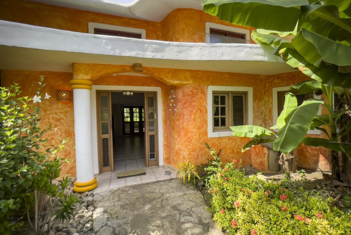 buyDRproperty Charming B&B entrance with orange stucco and tropical plants Sosua Real Estate