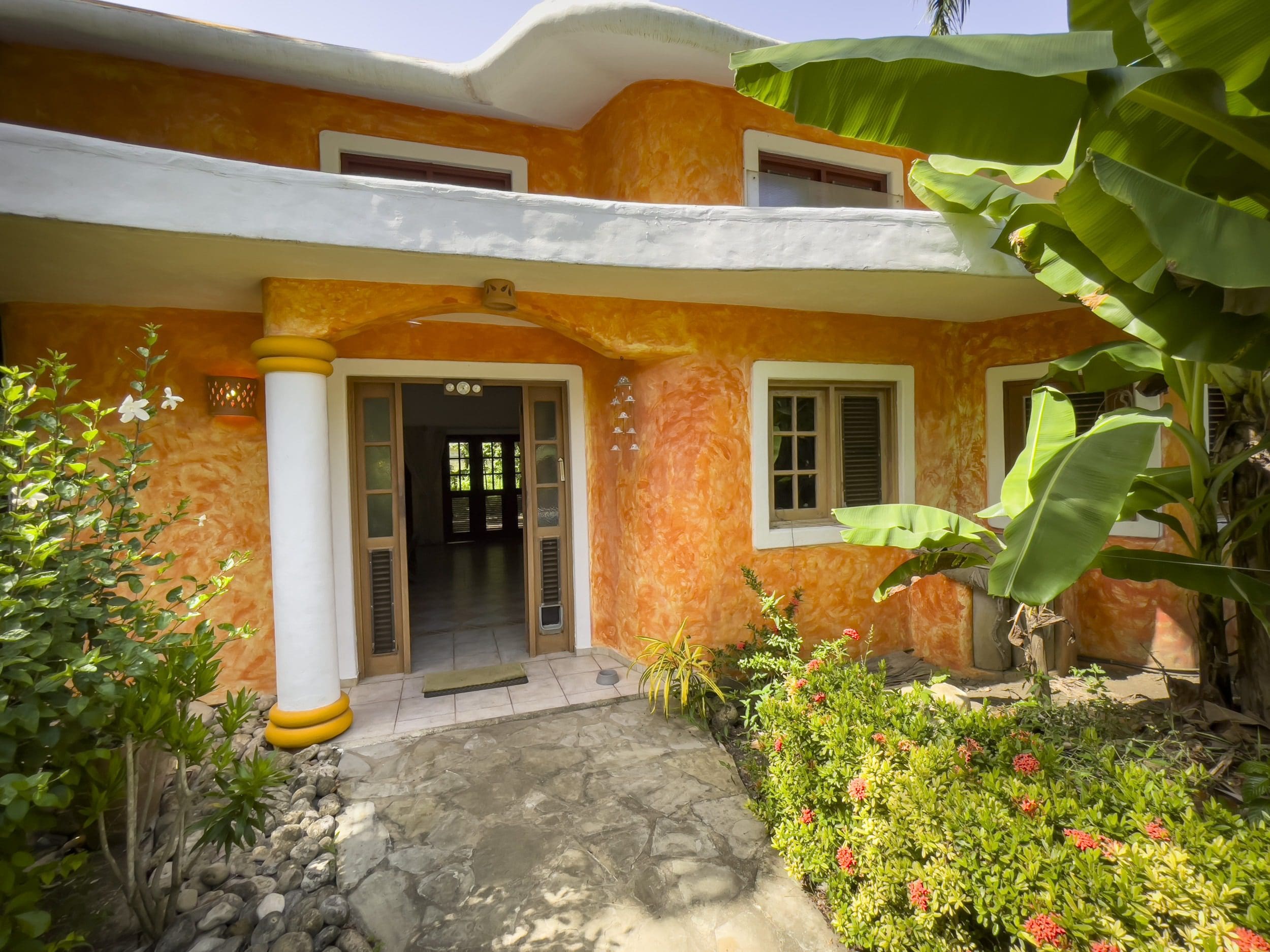 buyDRproperty Charming B&B entrance with orange stucco and tropical plants Sosua Real Estate