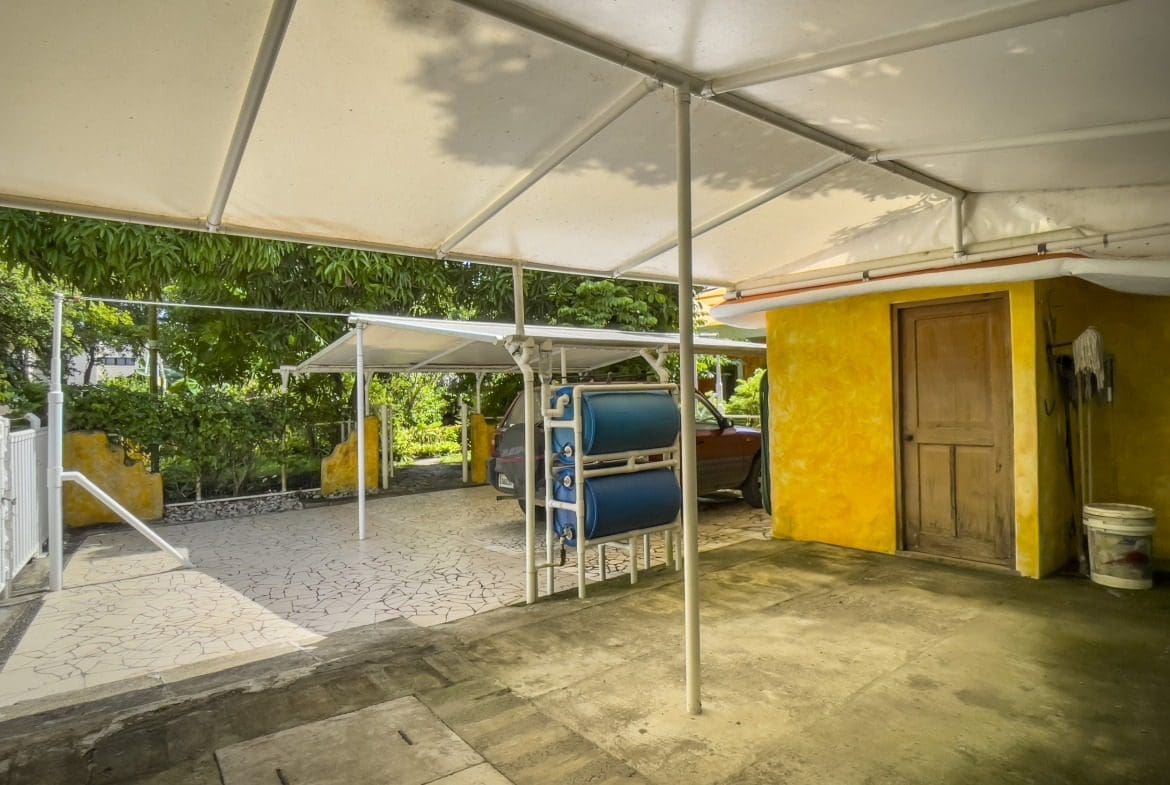 buyDRproperty Covered patio with car, blue water tanks, and yellow building, potentially a B&B. Sosua Real Estate