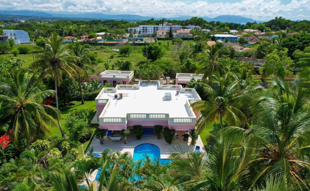 buyDRproperty Prime pink villa with a pool surrounded by lush tropical greenery. Sosua Real Estate