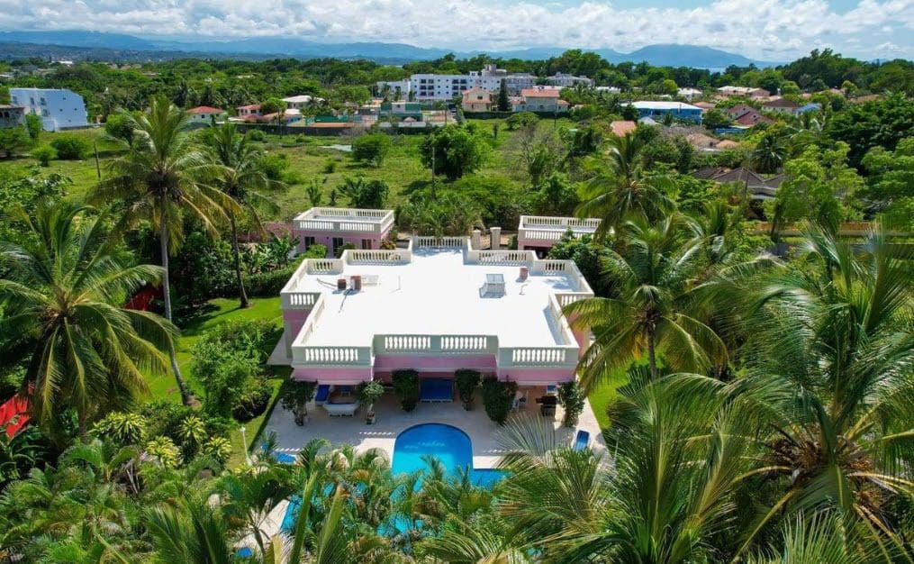 buyDRproperty Prime pink villa with a pool surrounded by lush tropical greenery. Sosua Real Estate