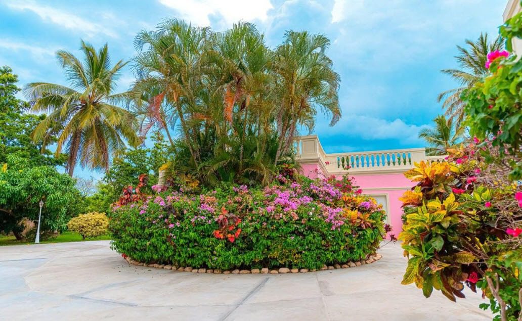 buyDRproperty Lush tropical villa entrance with palm trees and colorful flowers. Prime property. Sosua Real Estate