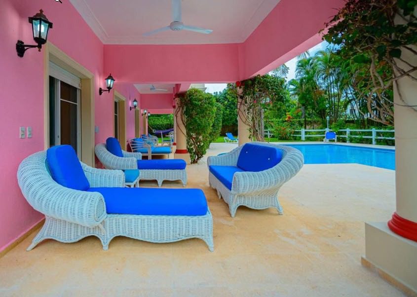 buyDRproperty Prime outdoor patio with white wicker furniture, blue cushions, and a pink exterior. Sosua Real Estate