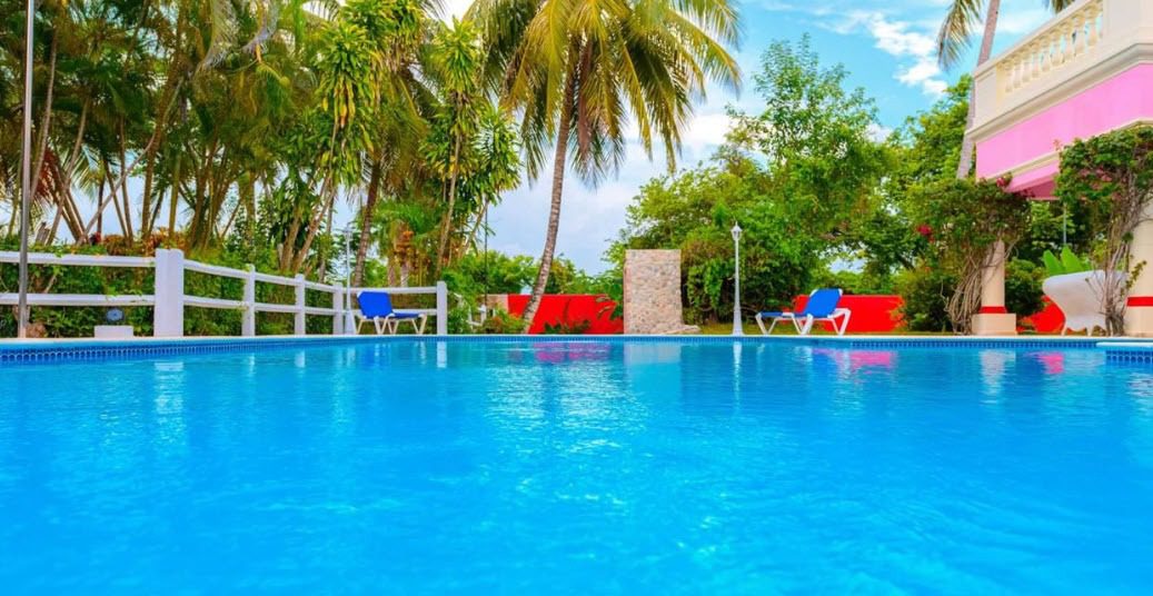 buyDRproperty Blue swimming pool at a prime villa with palm trees and a pink awning. Sosua Real Estate