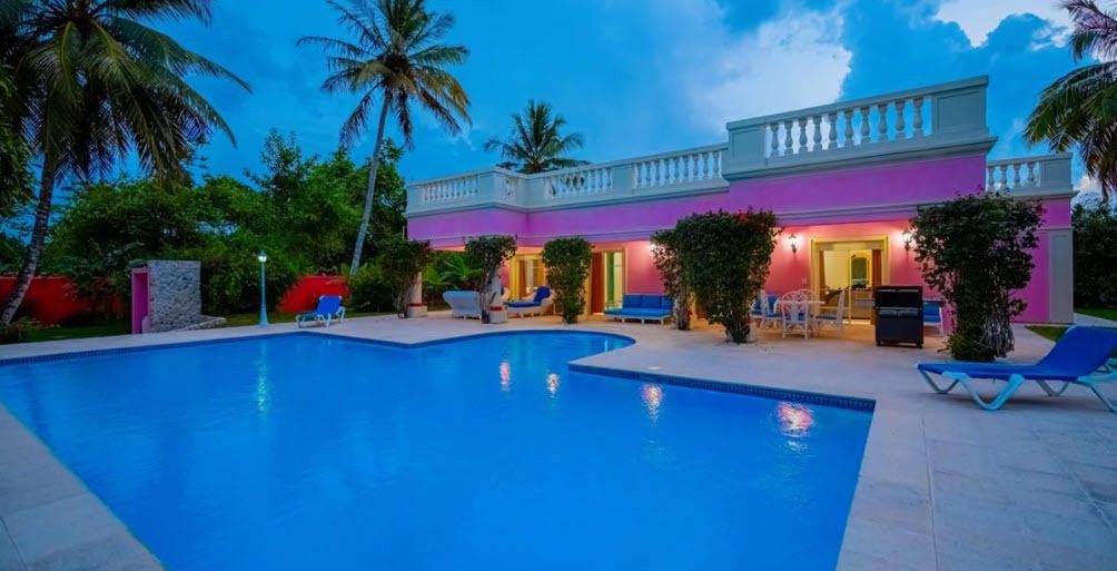 buyDRproperty Prime villa for sale with a pool, palm trees, and pink exterior. Sosua Real Estate