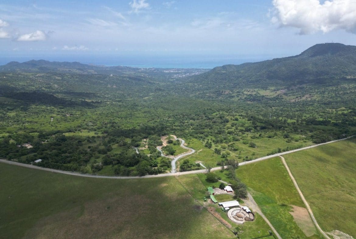 buyDRproperty Aerial view of a green valley with a road, mountains, and a farm, perfect for a stunning villa with mountain views. Sosua Real Estate