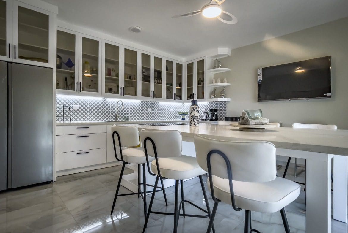 buyDRproperty Modern kitchen with white cabinets, bar stools, and a marble countertop. Offers modern comfort. Sosua Real Estate