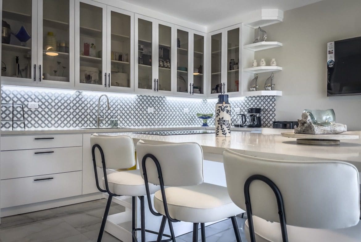 buyDRproperty Modern kitchen with white cabinets, bar stools, and a patterned backsplash. Offers modern comfort. Sosua Real Estate