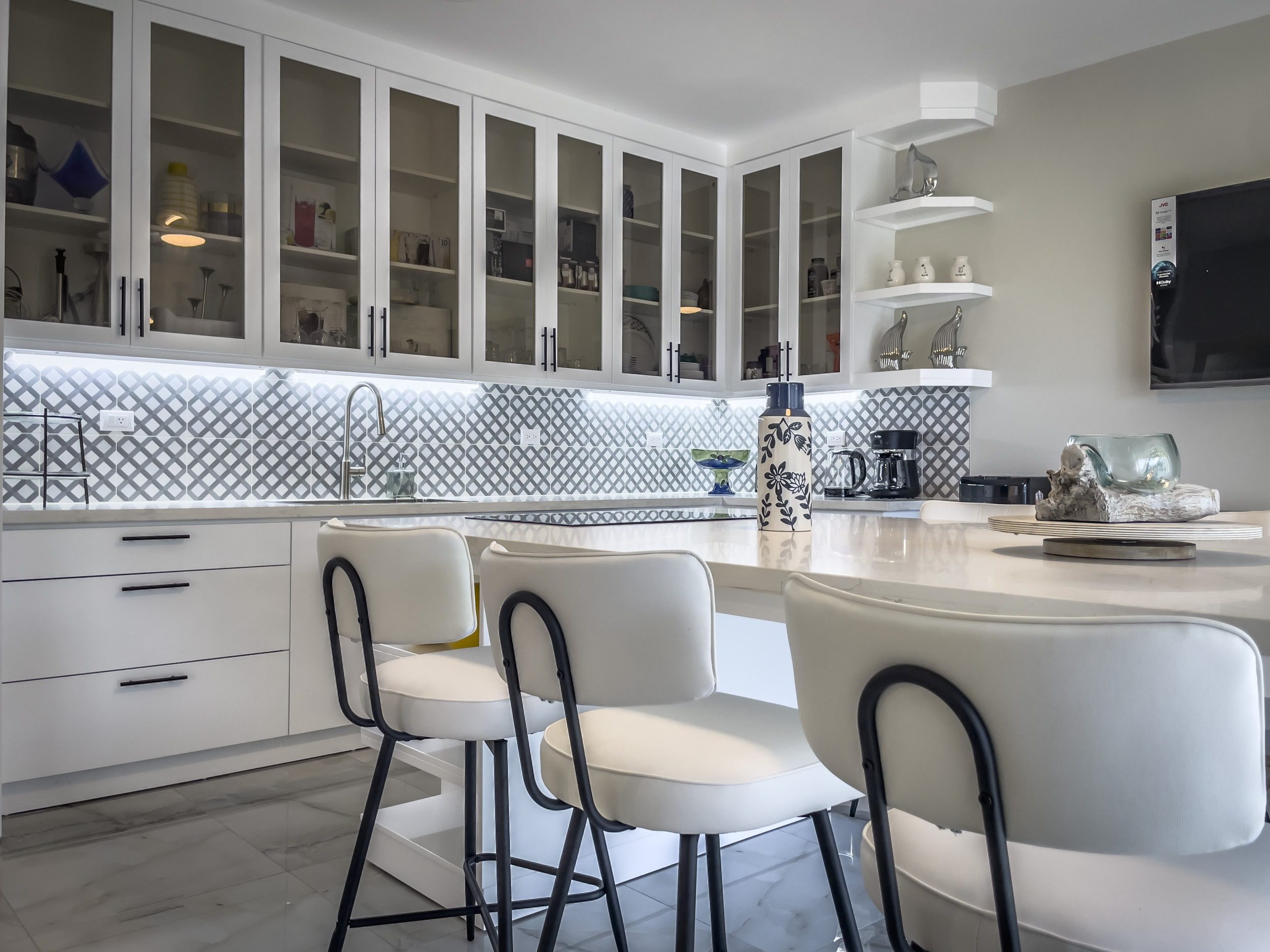buyDRproperty Modern kitchen with white cabinets, bar stools, and a patterned backsplash. Offers modern comfort. Sosua Real Estate