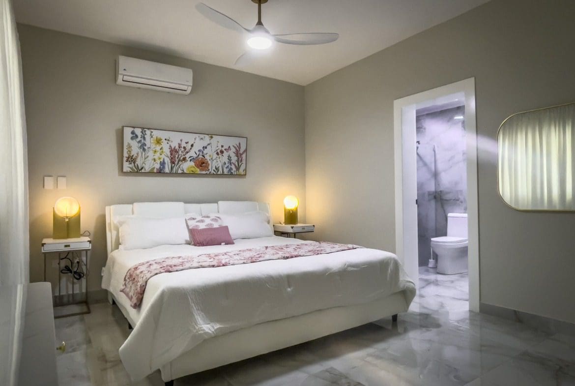 buyDRproperty Modern bedroom with a white bed, floral artwork, and marble floors, offering modern comfort. Sosua Real Estate