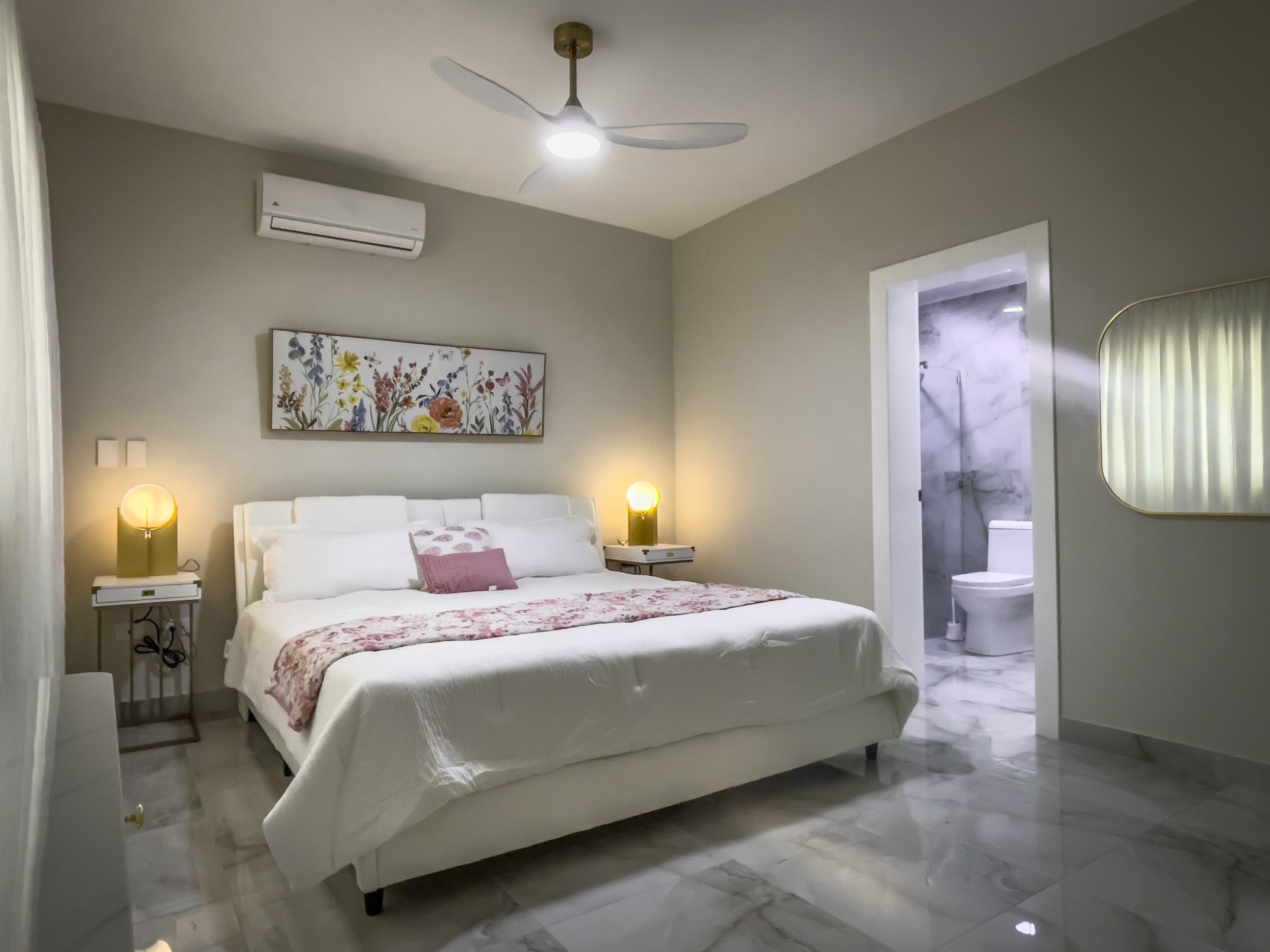 buyDRproperty Modern bedroom with a white bed, floral artwork, and marble floors, offering modern comfort. Sosua Real Estate