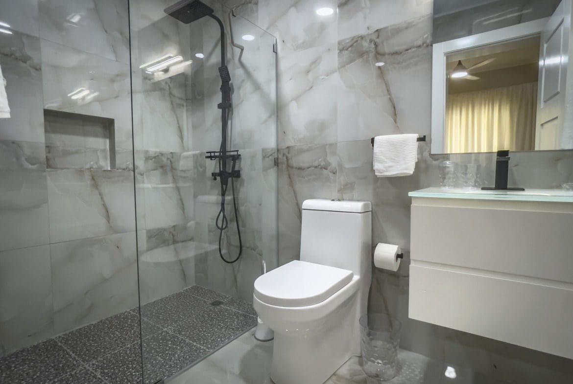 buyDRproperty Modern bathroom with glass shower, marble tile, and white toilet. Offers modern comfort. Sosua Real Estate