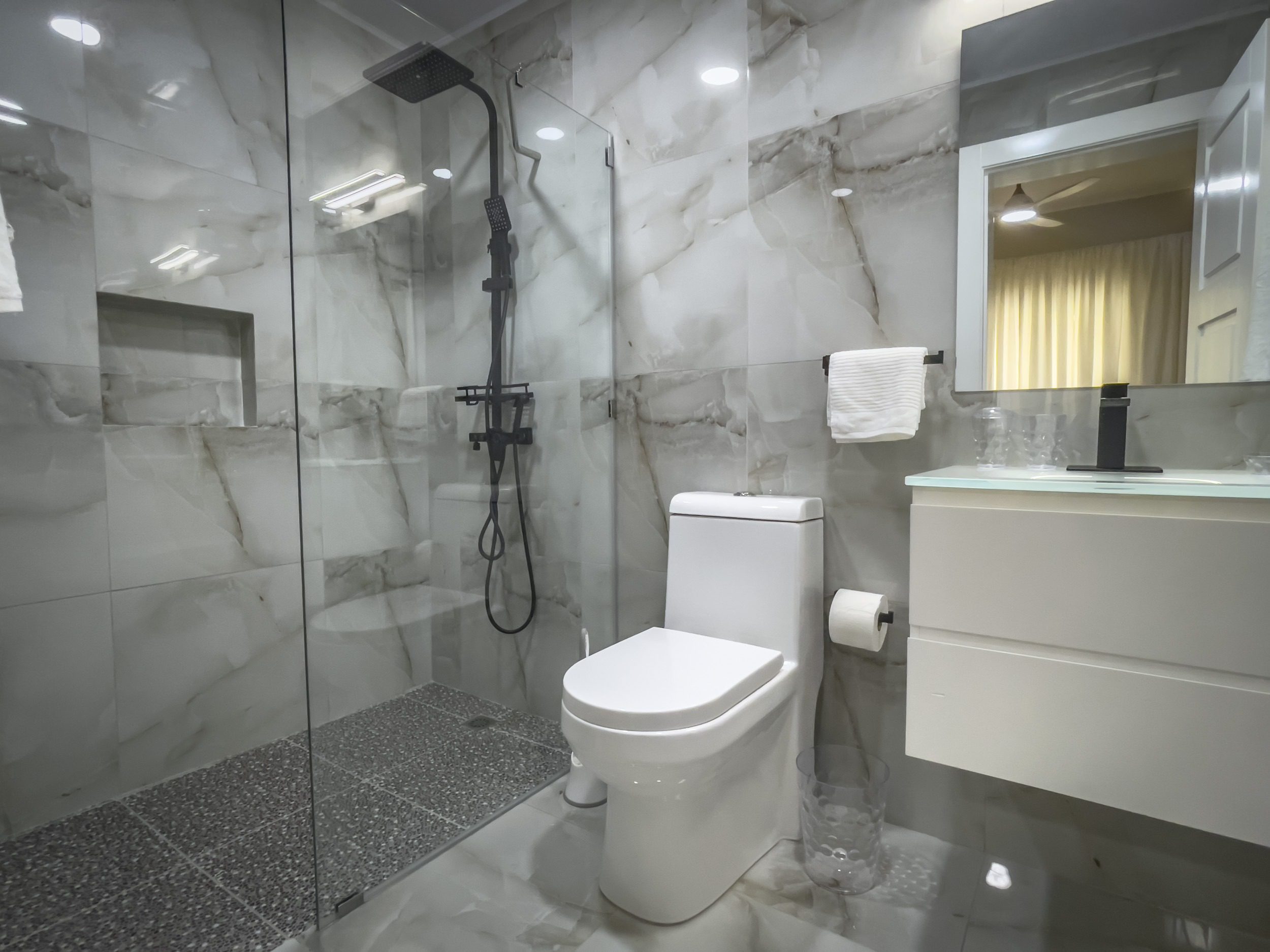 buyDRproperty Modern bathroom with glass shower, marble tile, and white toilet. Offers modern comfort. Sosua Real Estate