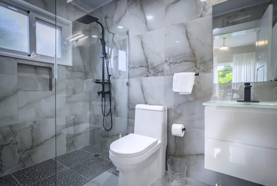 buyDRproperty Modern bathroom with marble tile, black shower fixtures, and a white toilet. Offers modern comfort. Sosua Real Estate