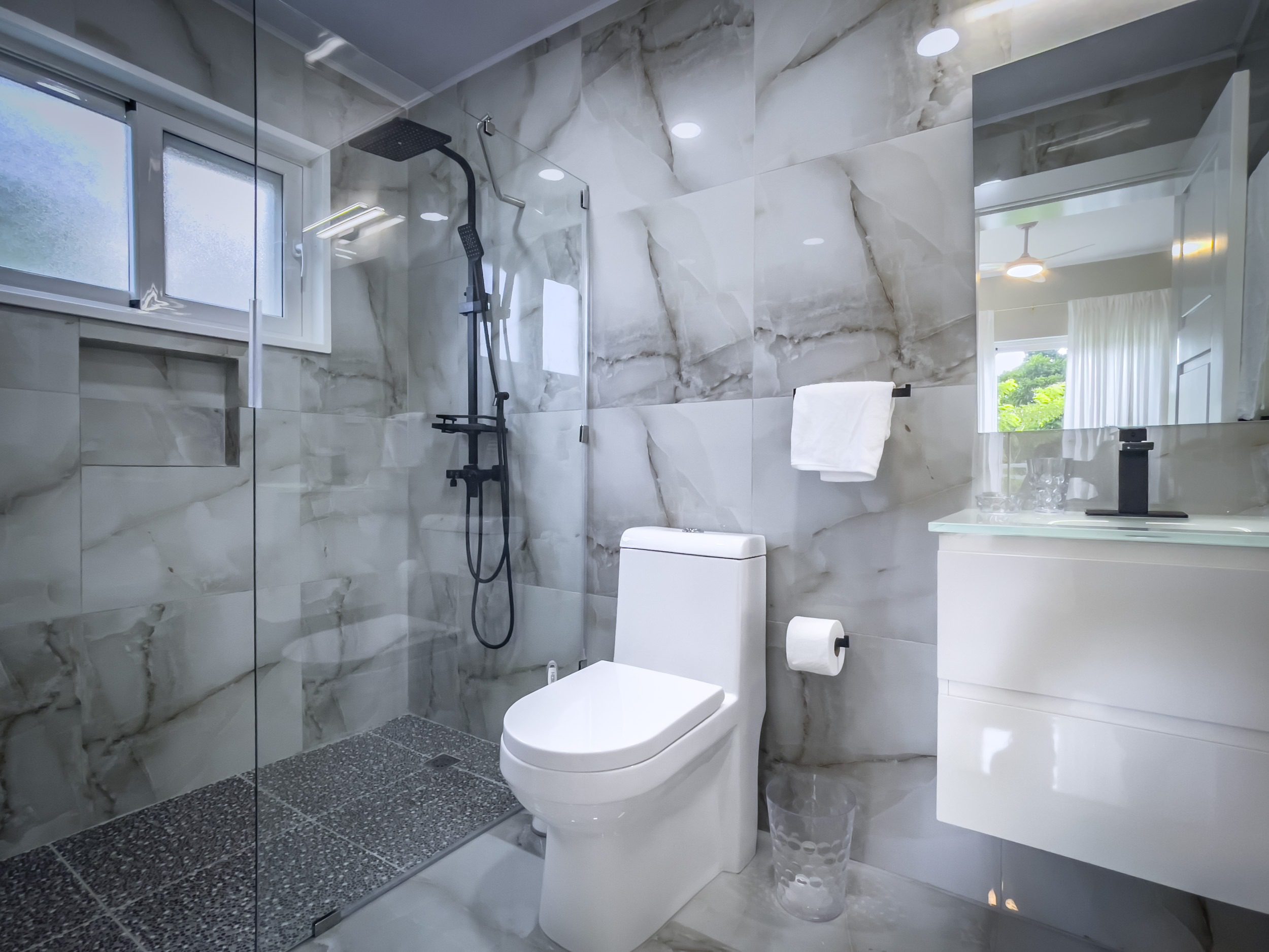 buyDRproperty Modern bathroom with marble tile, black shower fixtures, and a white toilet. Offers modern comfort. Sosua Real Estate