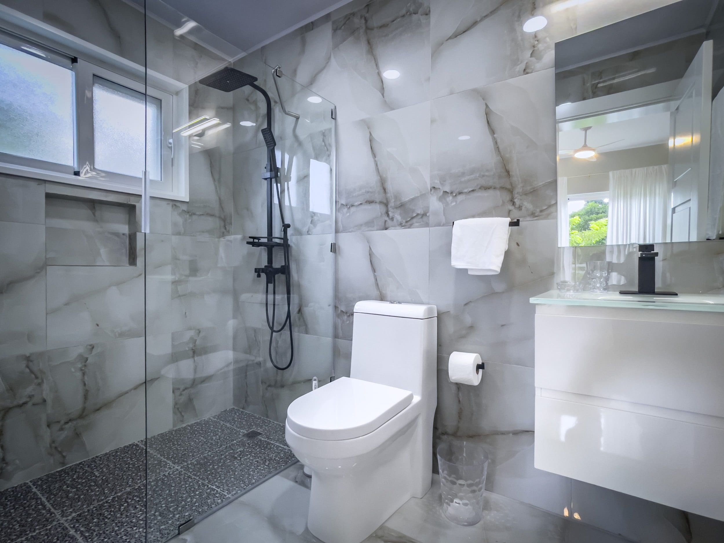 buyDRproperty Modern bathroom with marble tile, black shower fixtures, and a white toilet. Offers modern comfort. Sosua Real Estate