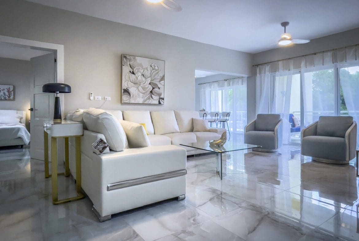 buyDRproperty Modern living room with white sofa, glass table, and two armchairs, offering modern comfort. Sosua Real Estate
