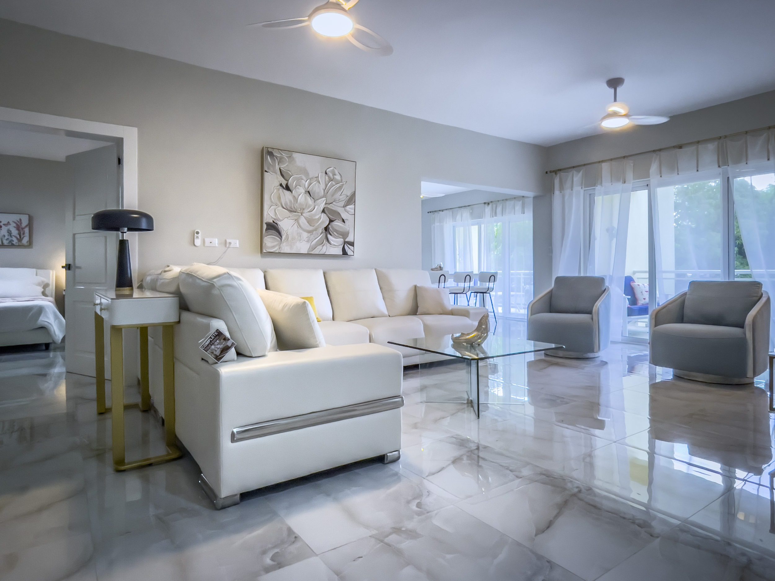buyDRproperty Modern living room with white sofa, glass table, and two armchairs, offering modern comfort. Sosua Real Estate