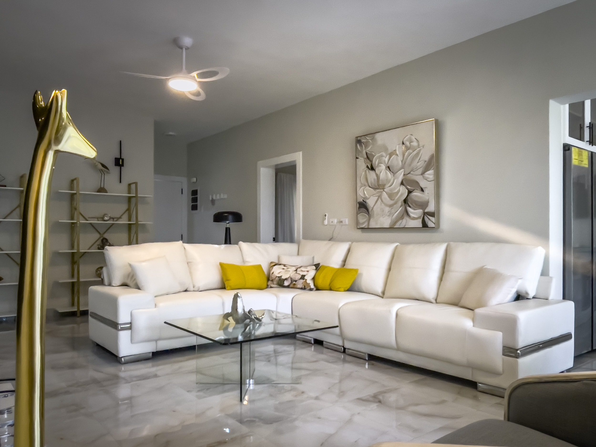 buyDRproperty Modern living room with white sectional sofa, glass coffee table, and floral artwork. Sosua Real Estate