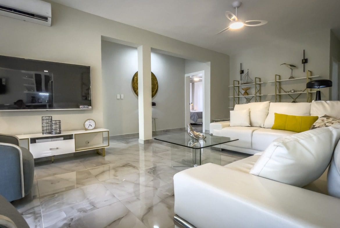buyDRproperty Modern living room with white leather sofa, glass coffee table, and marble flooring. Offering Modern Comfort. Sosua Real Estate