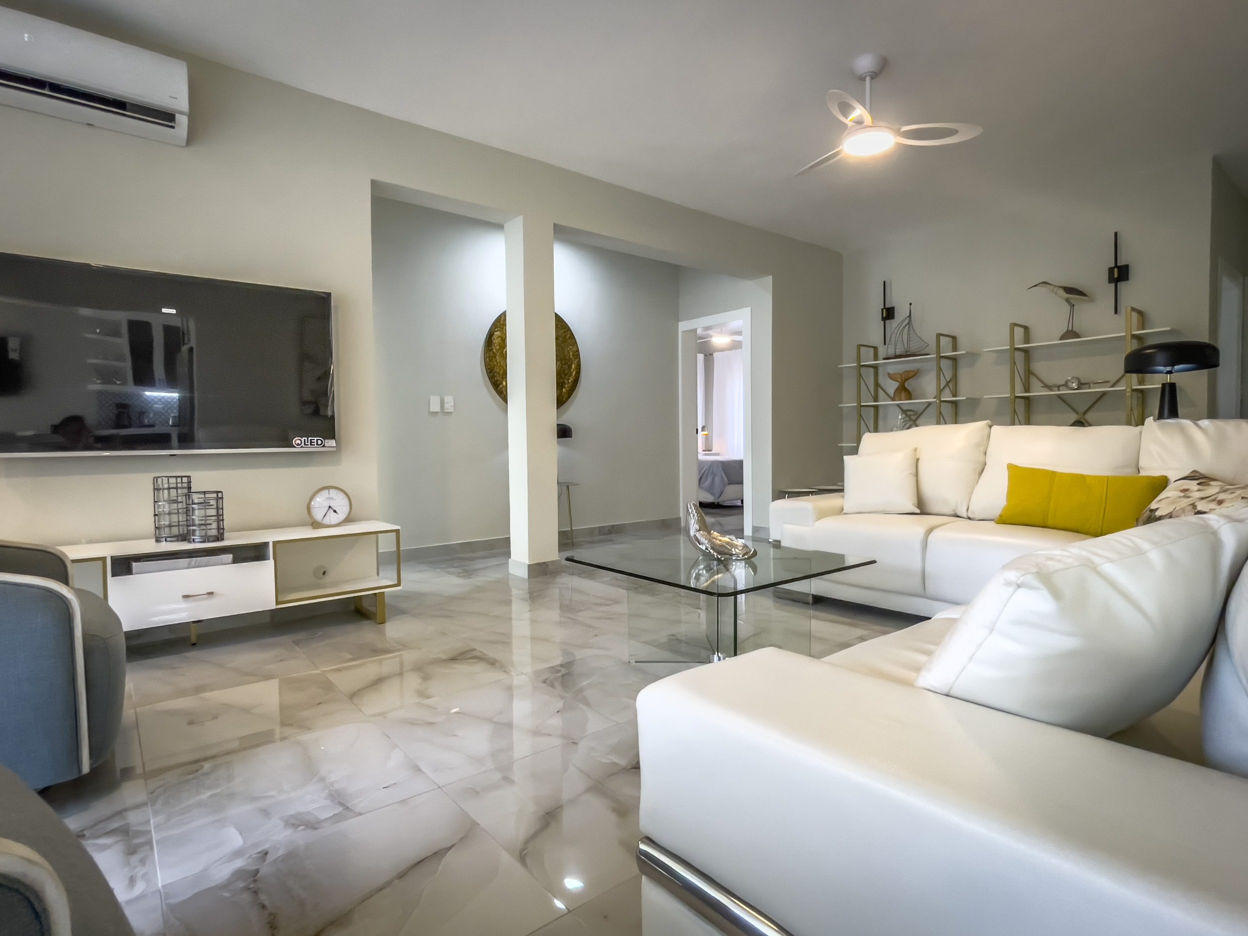 buyDRproperty Modern living room with white leather sofa, glass coffee table, and marble flooring. Offering Modern Comfort. Sosua Real Estate