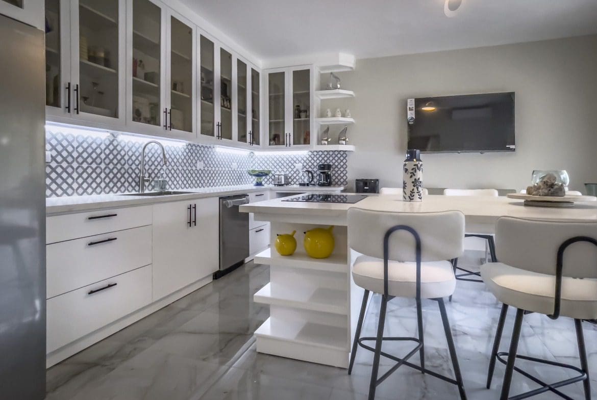 buyDRproperty Modern white kitchen with glass-front cabinets and a breakfast bar, offering modern comfort. Sosua Real Estate