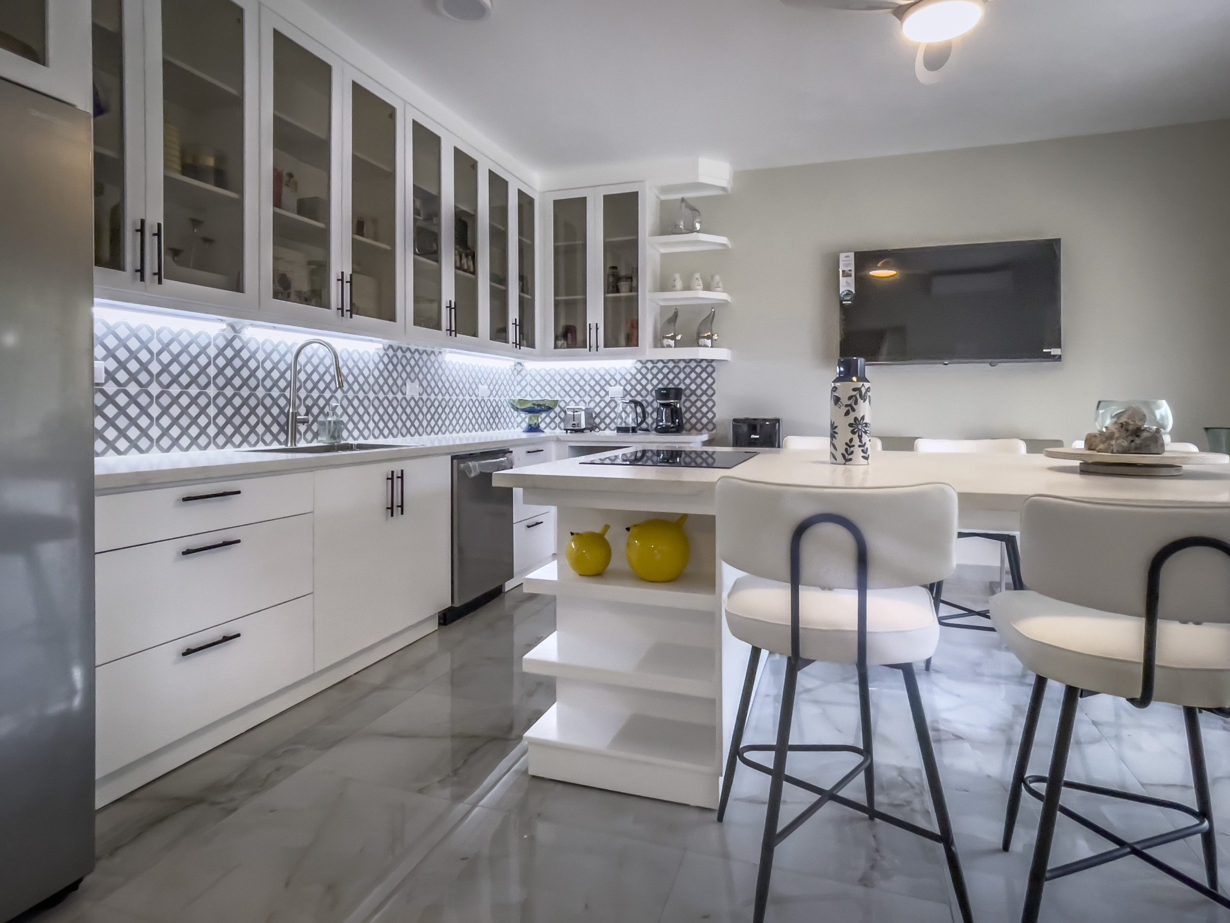 buyDRproperty Modern white kitchen with glass-front cabinets and a breakfast bar, offering modern comfort. Sosua Real Estate