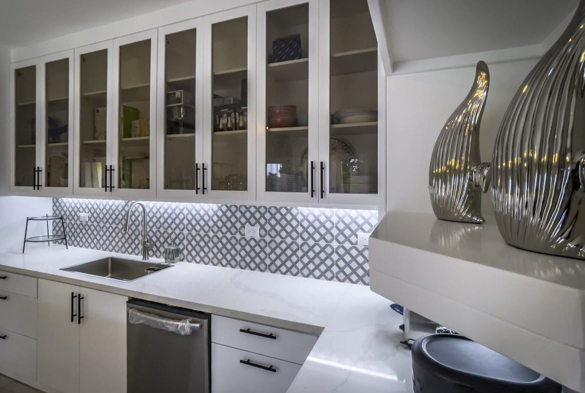 buyDRproperty Modern kitchen with white cabinets, glass-front uppers, and geometric backsplash. Offers modern comfort. Sosua Real Estate