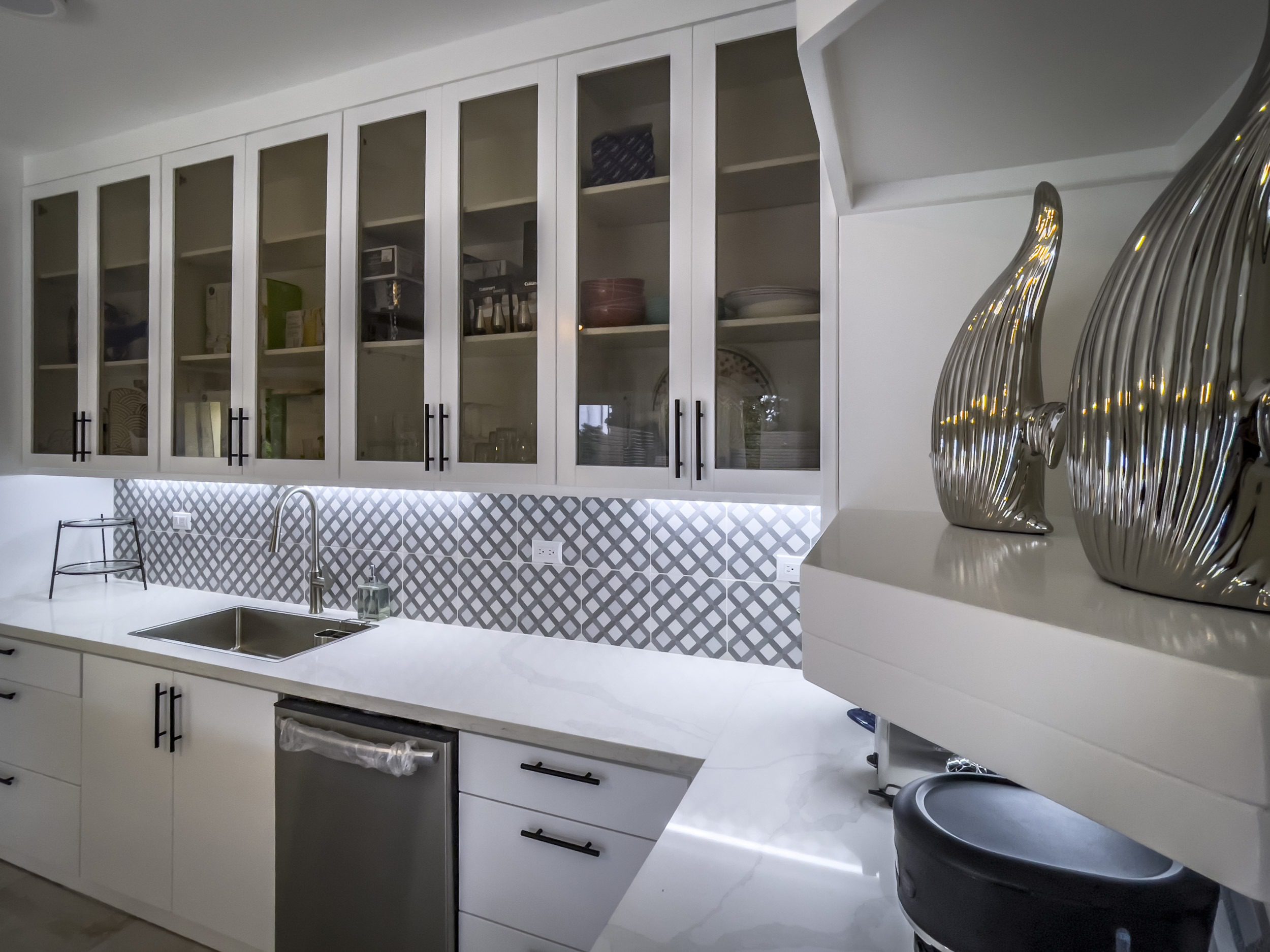 buyDRproperty Modern kitchen with white cabinets, glass-front uppers, and geometric backsplash. Offers modern comfort. Sosua Real Estate