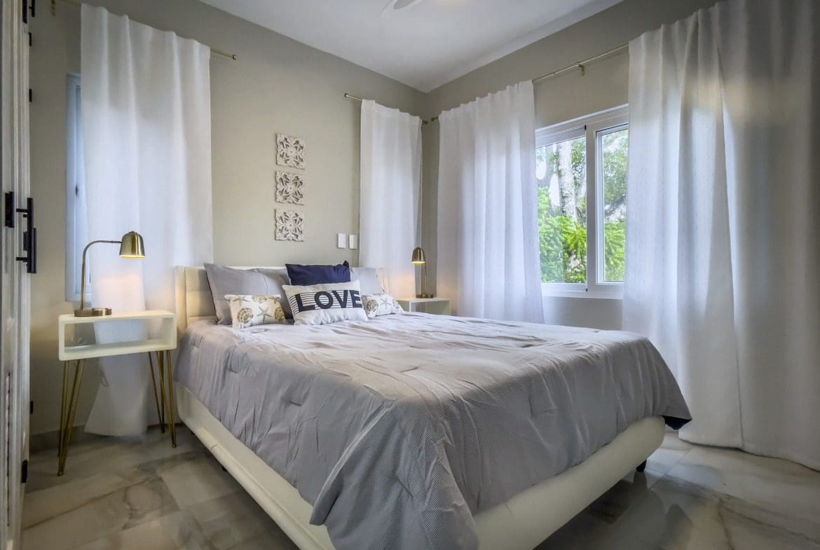buyDRproperty Modern bedroom with a gray comforter, white curtains, and a "LOVE" pillow. Sosua Real Estate