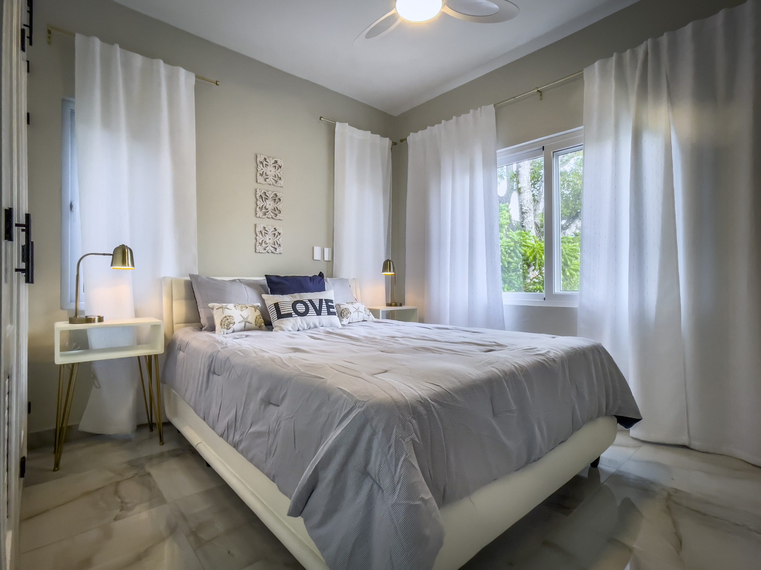 buyDRproperty Modern bedroom with a gray comforter, white curtains, and a "LOVE" pillow. Sosua Real Estate