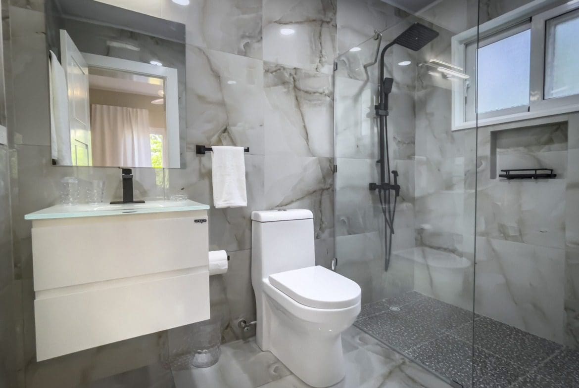 buyDRproperty Modern bathroom with marble tile, glass shower, and white toilet for modern comfort. Sosua Real Estate