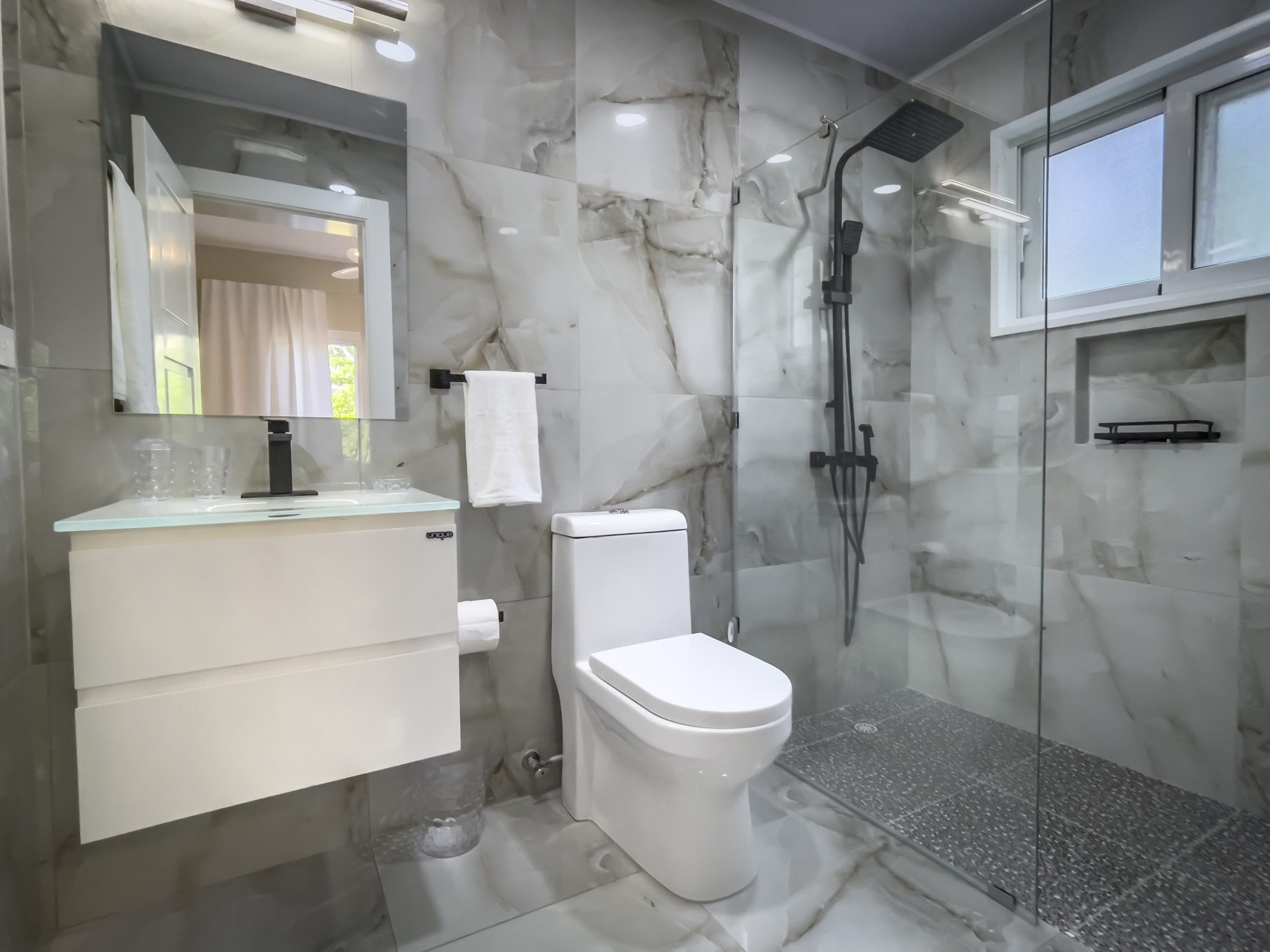 buyDRproperty Modern bathroom with marble tile, glass shower, and white toilet for modern comfort. Sosua Real Estate