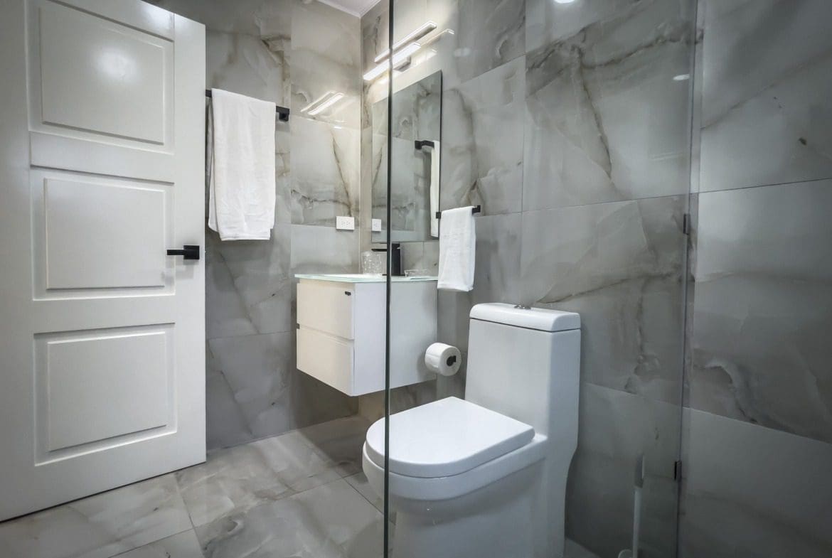 buyDRproperty Modern bathroom with marble tile, white toilet, and glass shower enclosure. Sosua Real Estate