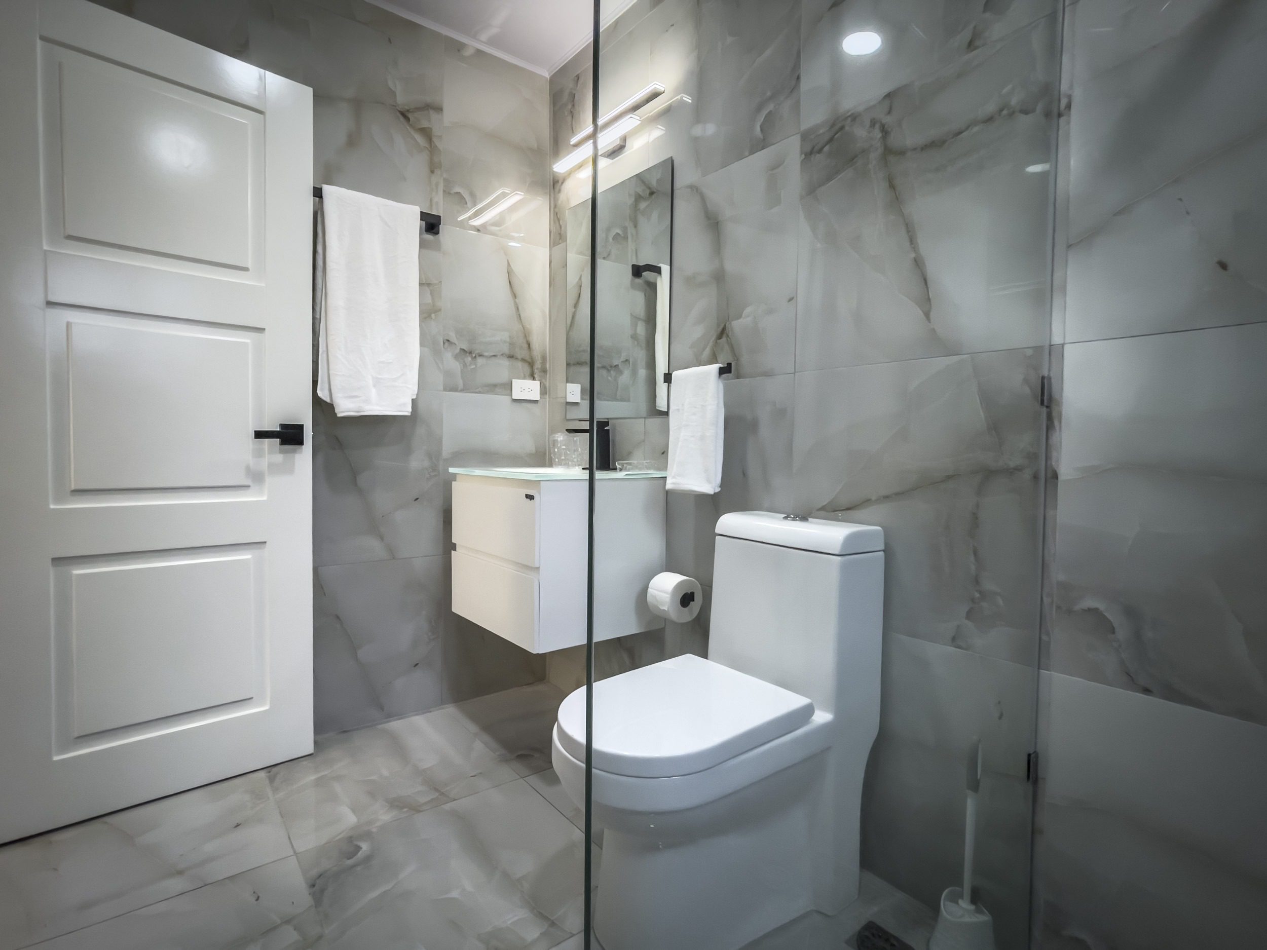 buyDRproperty Modern bathroom with marble tile, white toilet, and glass shower enclosure. Sosua Real Estate
