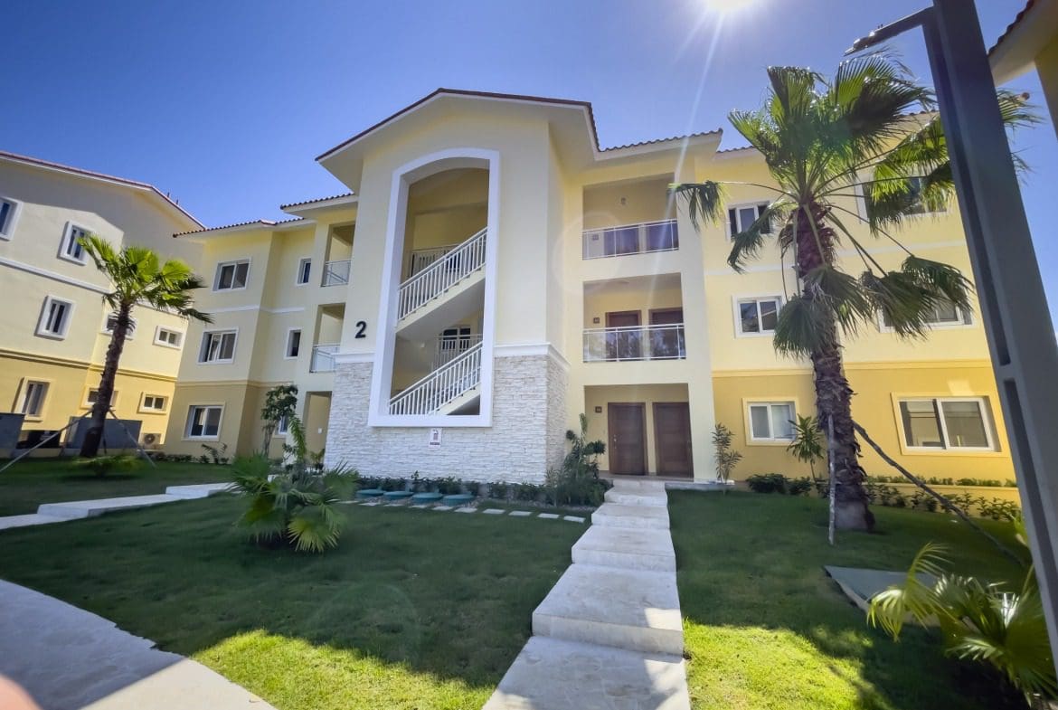 buyDRproperty Exterior view of a modern condo building with palm trees and a staircase. Sosua Real Estate