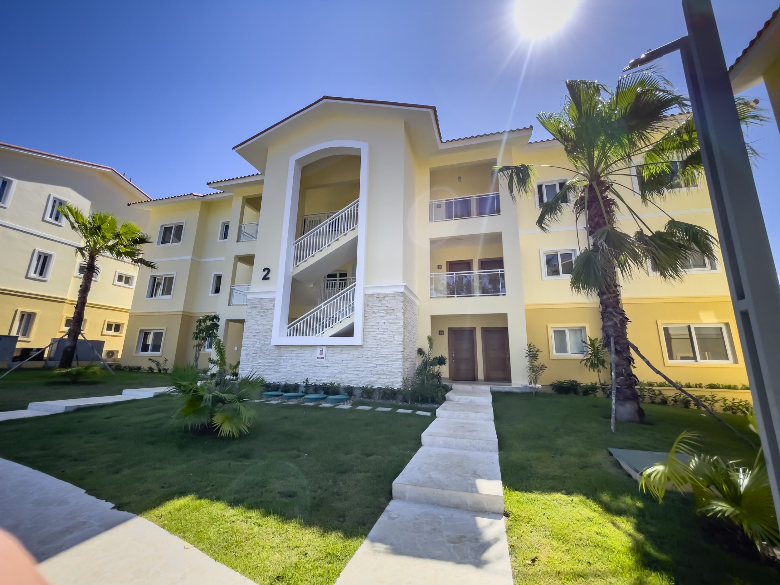 buyDRproperty Exterior view of a modern condo building with palm trees and a staircase. Sosua Real Estate