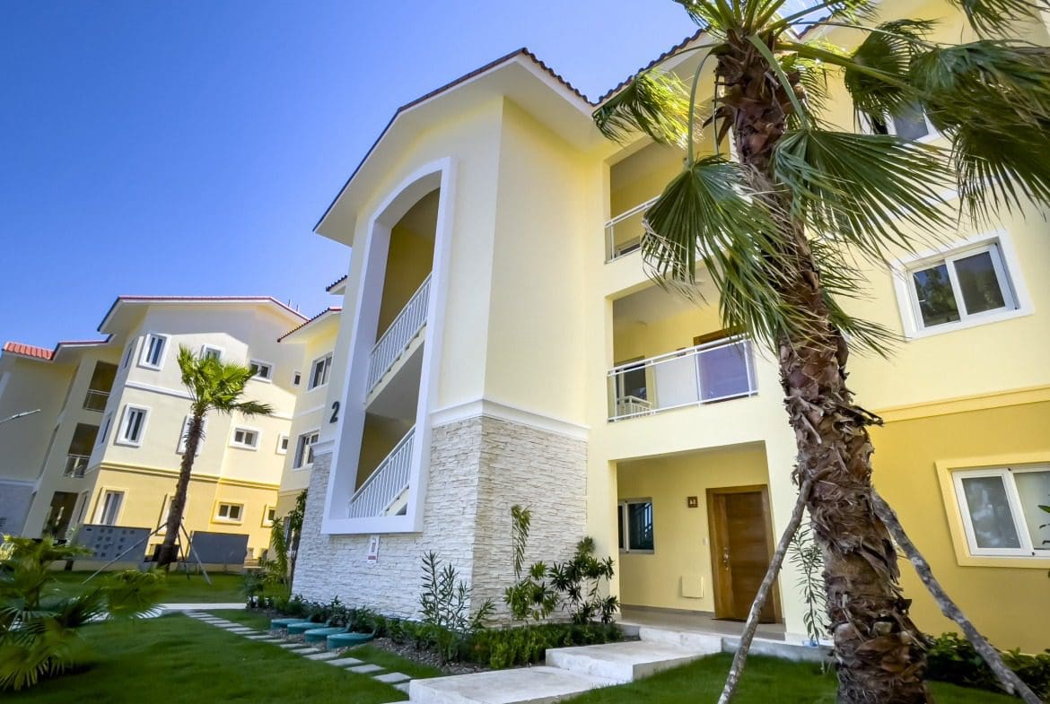 buyDRproperty Exterior of a modern condo building with palm trees and a bright blue sky. Sosua Real Estate