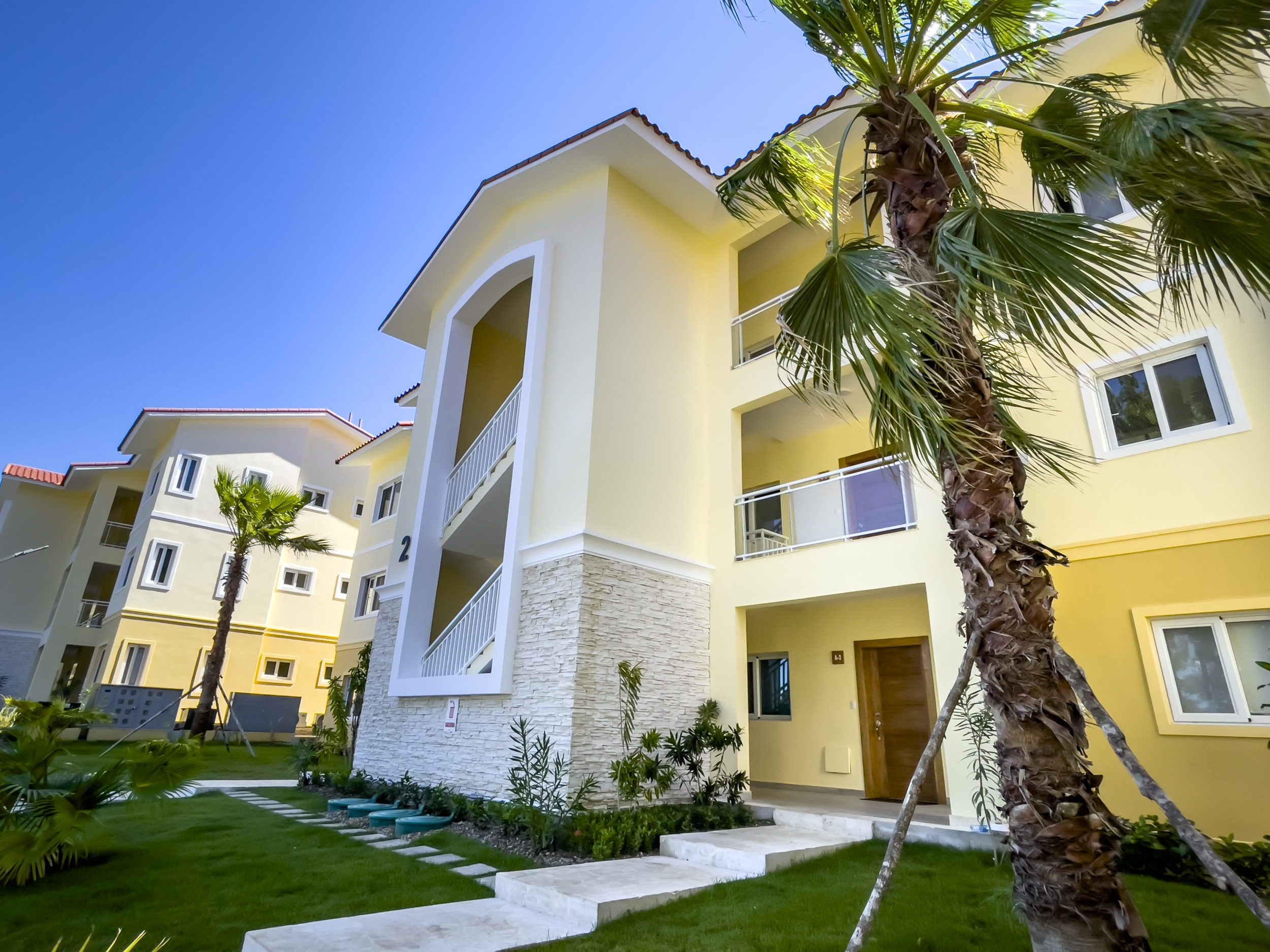 buyDRproperty Exterior of a modern condo building with palm trees and a bright blue sky. Sosua Real Estate