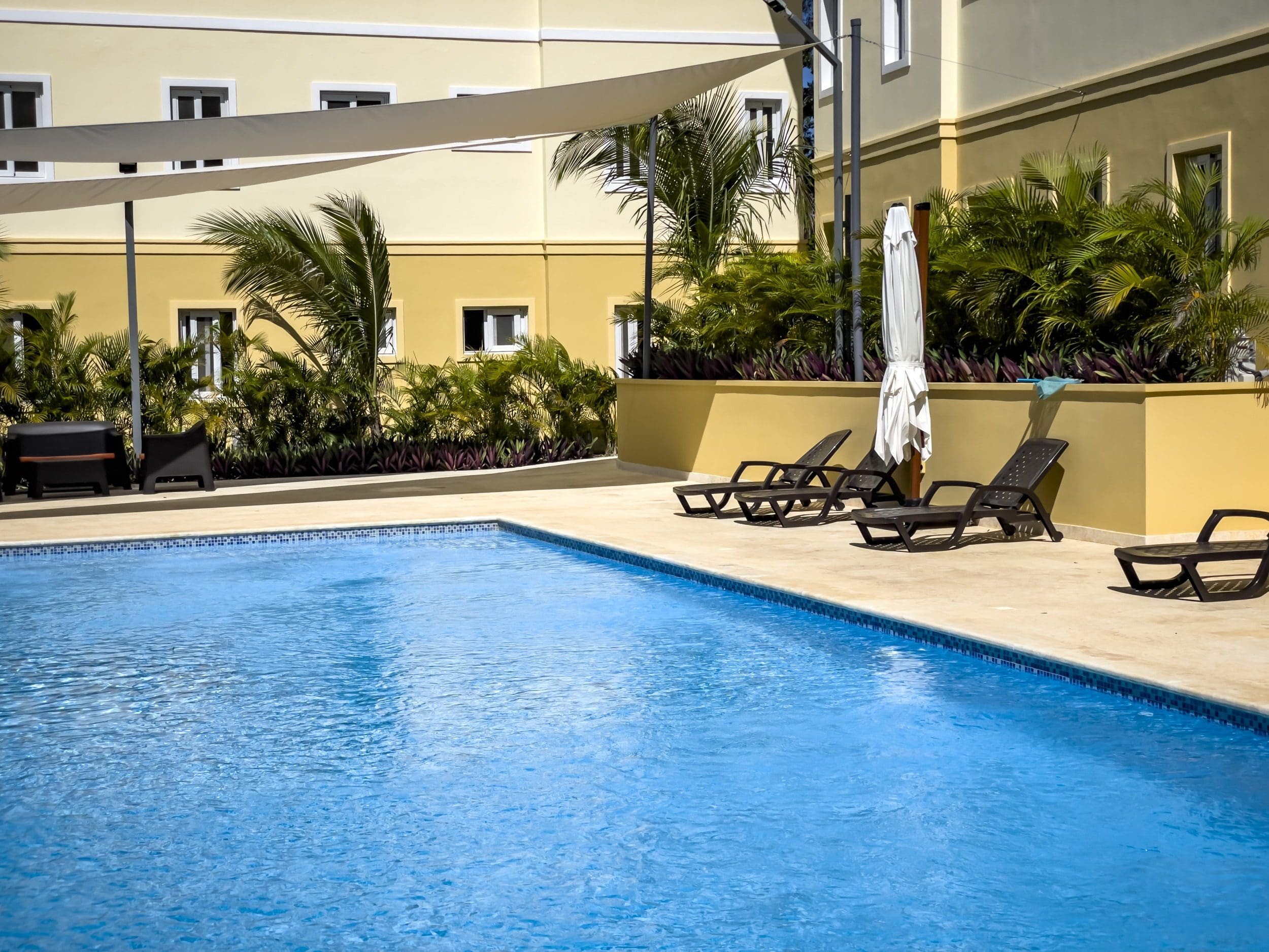 buyDRproperty Poolside lounge chairs with palm trees and a building in the background. Sosua Real Estate